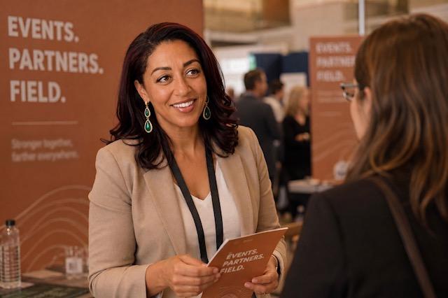 Charla Session-Reed talking with an attendee at an Events. Partners. Field. tradeshow booth.